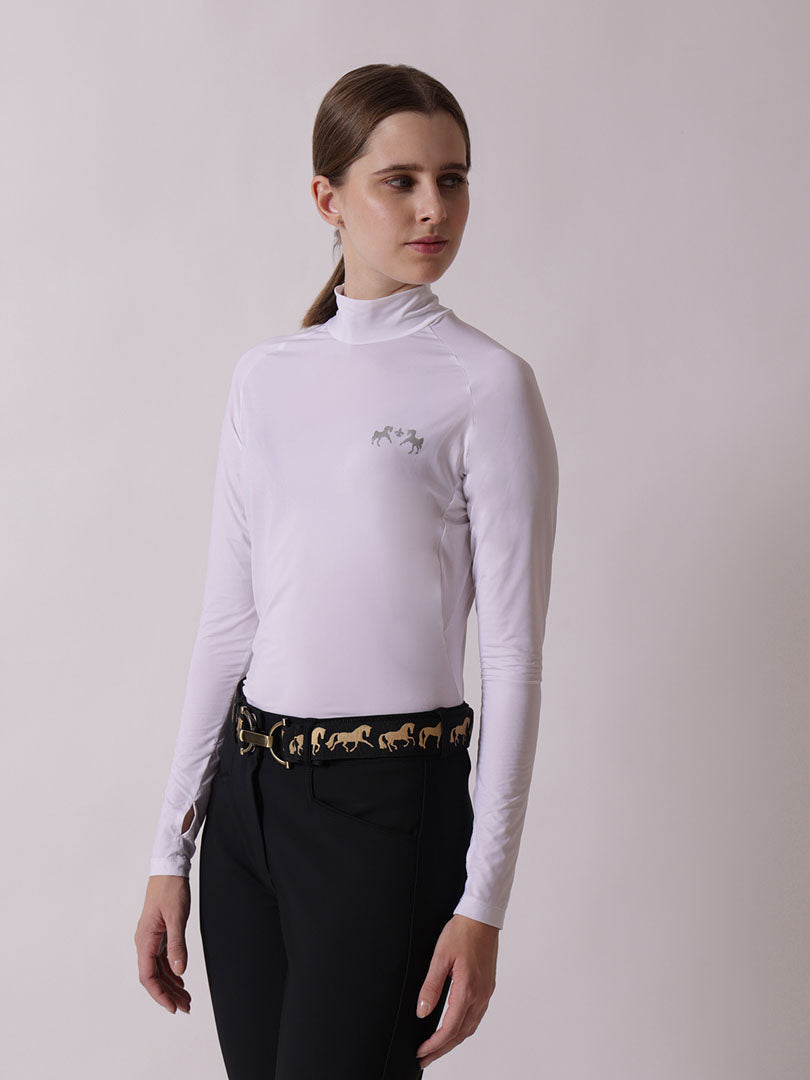 Woman wearing a white long-sleeve top with horse design and black pants on a plain background