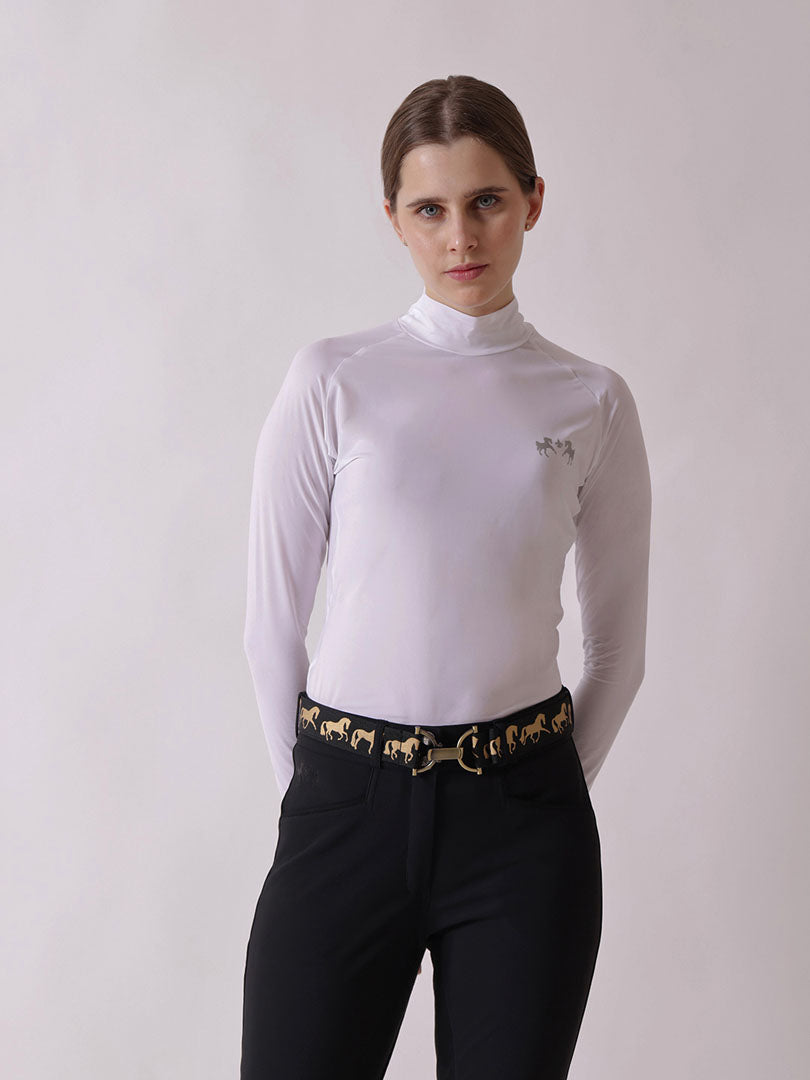 Woman wearing a white long-sleeve top and black pants with a gold belt against a plain background
