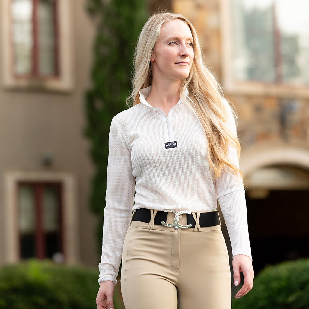 Woman in equestrian attire standing outdoors with a blurred background