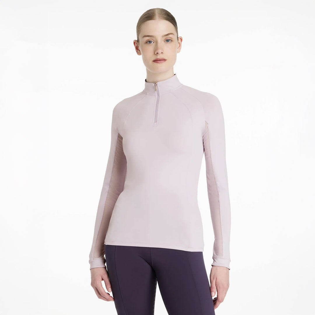 Woman wearing a light pink long-sleeve top with a quarter zip on a white background