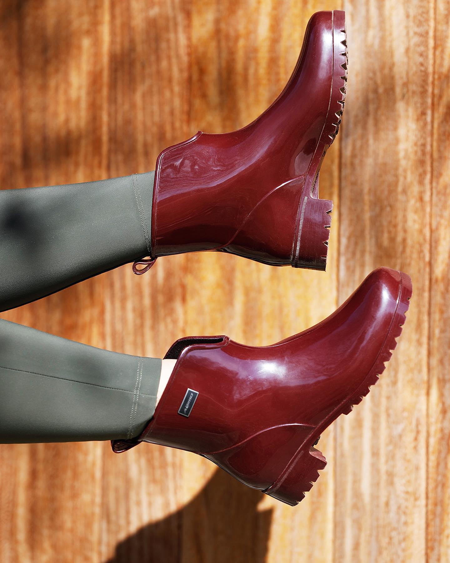 Red rubber paddock boots worn with green breeches on a wooden floor.