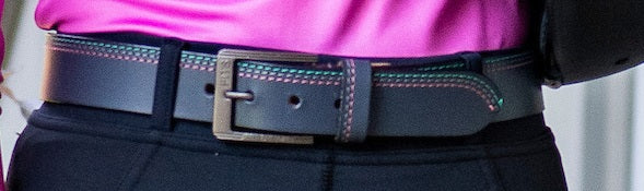 Close-up of a person wearing a black belt with decorative stitching on a blurred background