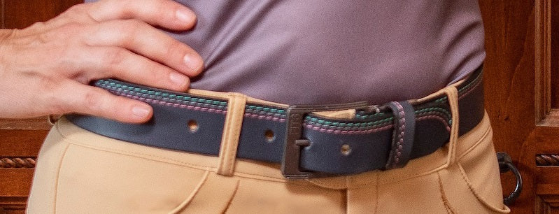 Person wearing a belt with a visible buckle, standing against a wooden background.