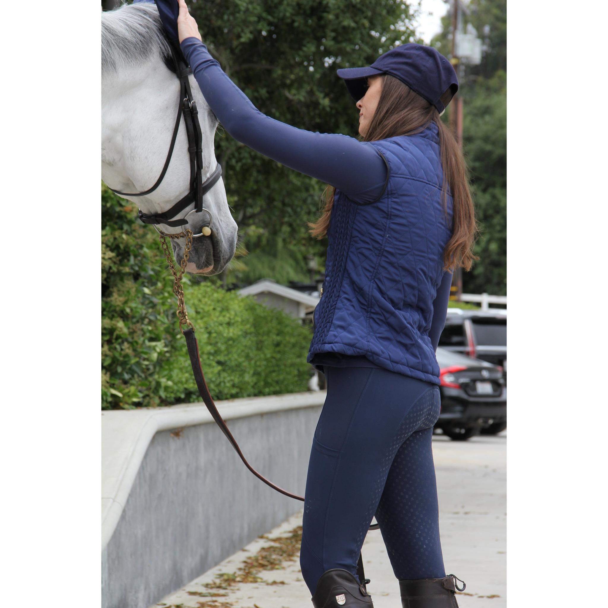 Person in blue equestrian gear interacting with a white horse on a path.
