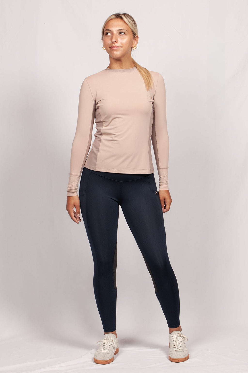 Woman wearing a beige long-sleeve top and black leggings on a white background