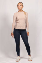 Woman wearing a beige long-sleeve top and black leggings on a white background