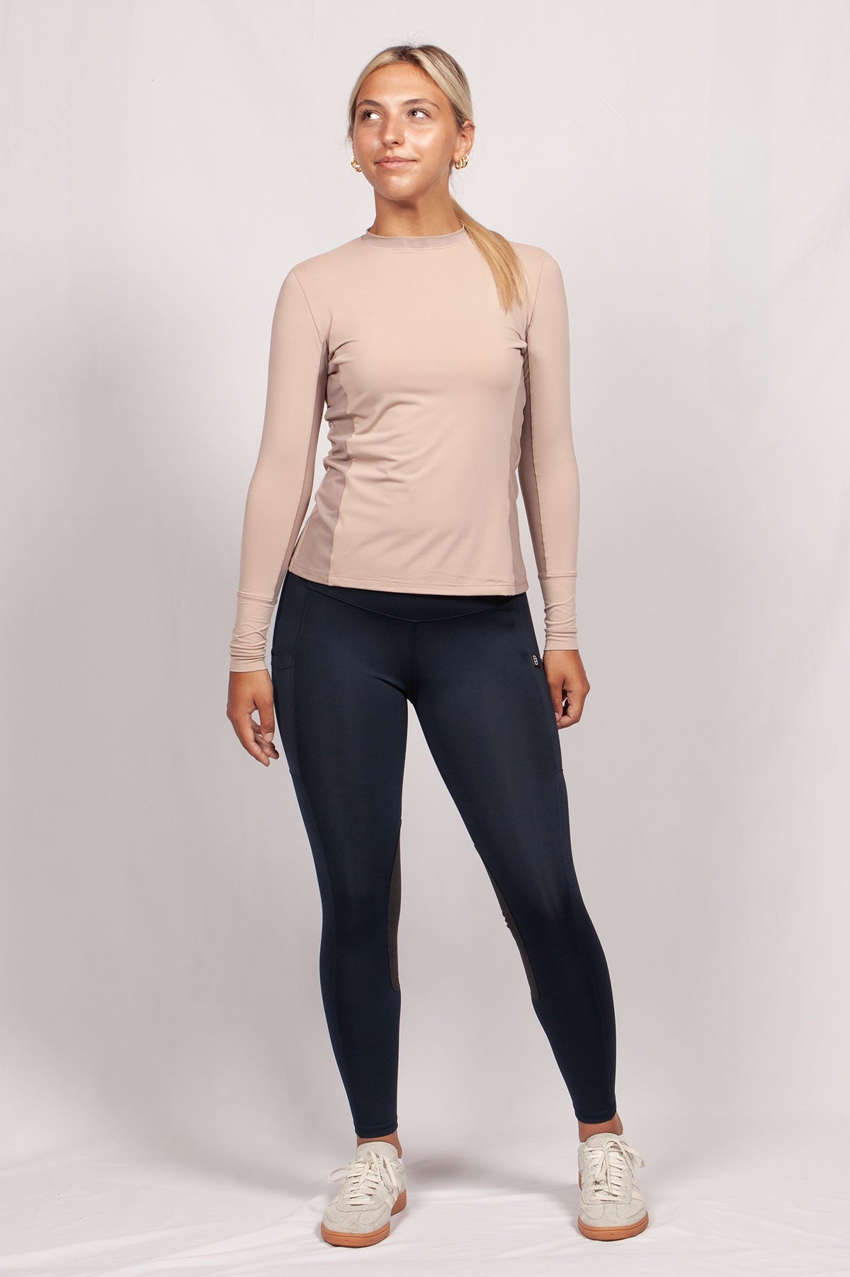 Woman wearing a beige long-sleeve top and black leggings on a white background
