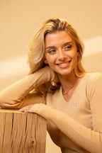Woman in a beige sweater leaning against a wooden surface with a neutral background