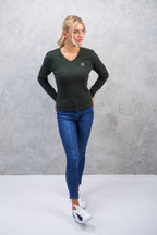 Woman wearing a dark green long-sleeve top and blue jeans against a gray background