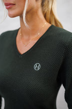 Person wearing a dark green textured long-sleeve top with a logo on a plain background