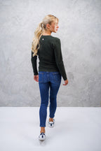 Woman wearing a dark green sweater and blue jeans against a gray background