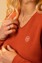 Person wearing an orange sweater with a logo, adjusting their collar.
