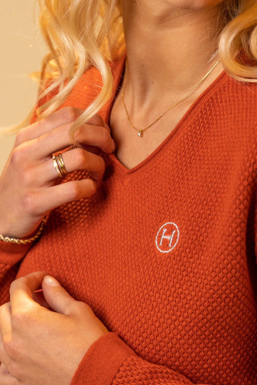 Person wearing an orange sweater with a logo, adjusting their collar.