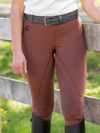 Person wearing brown riding pants with a belt, standing near a wooden fence.