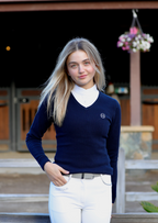 Person wearing a navy sweater with a logo and white pants outdoors.