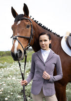 Woman in equestrian attire standing next to a brown horse in an outdoor setting.