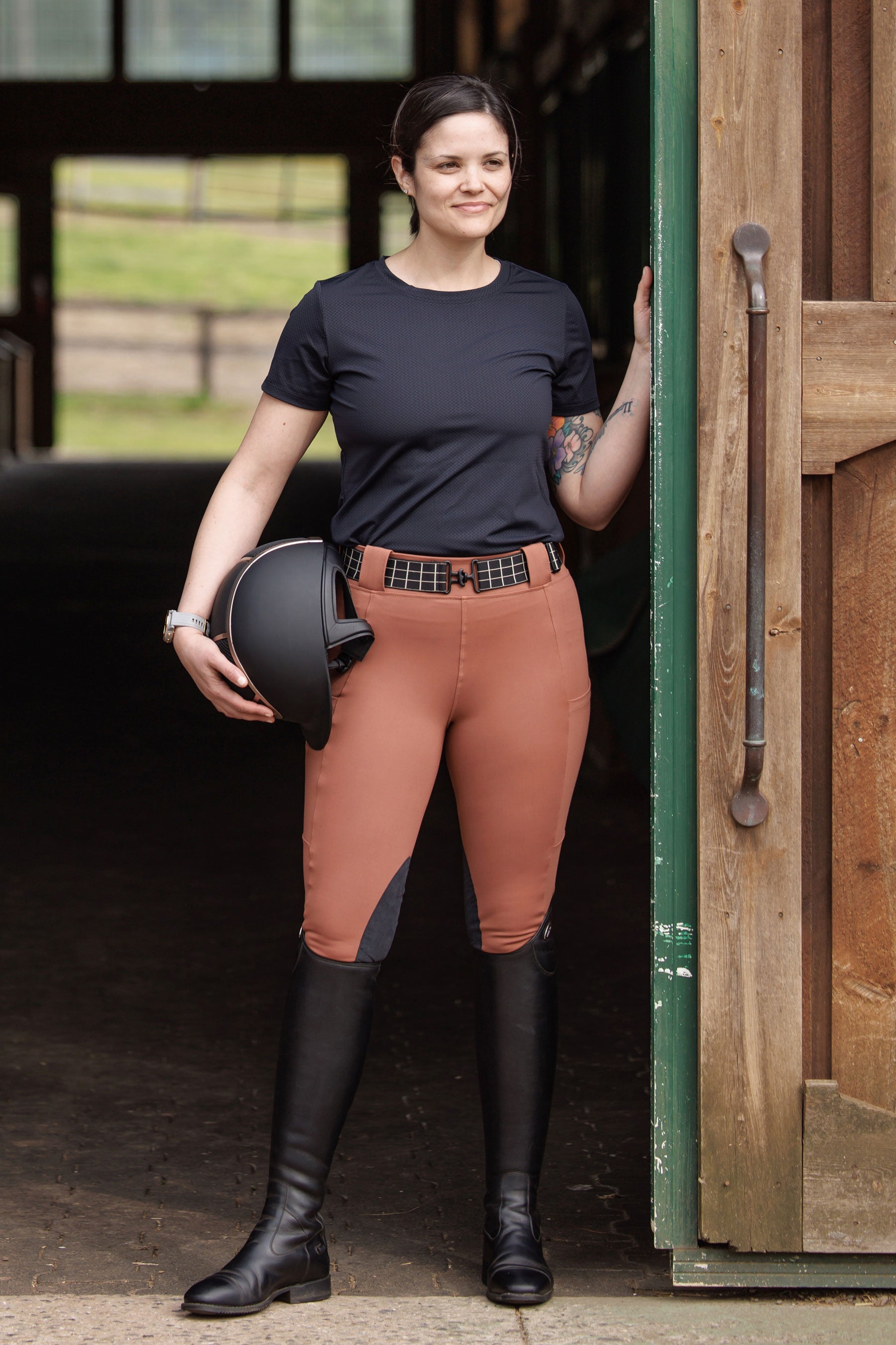 Woman in equestrian attire standing in a stable doorway