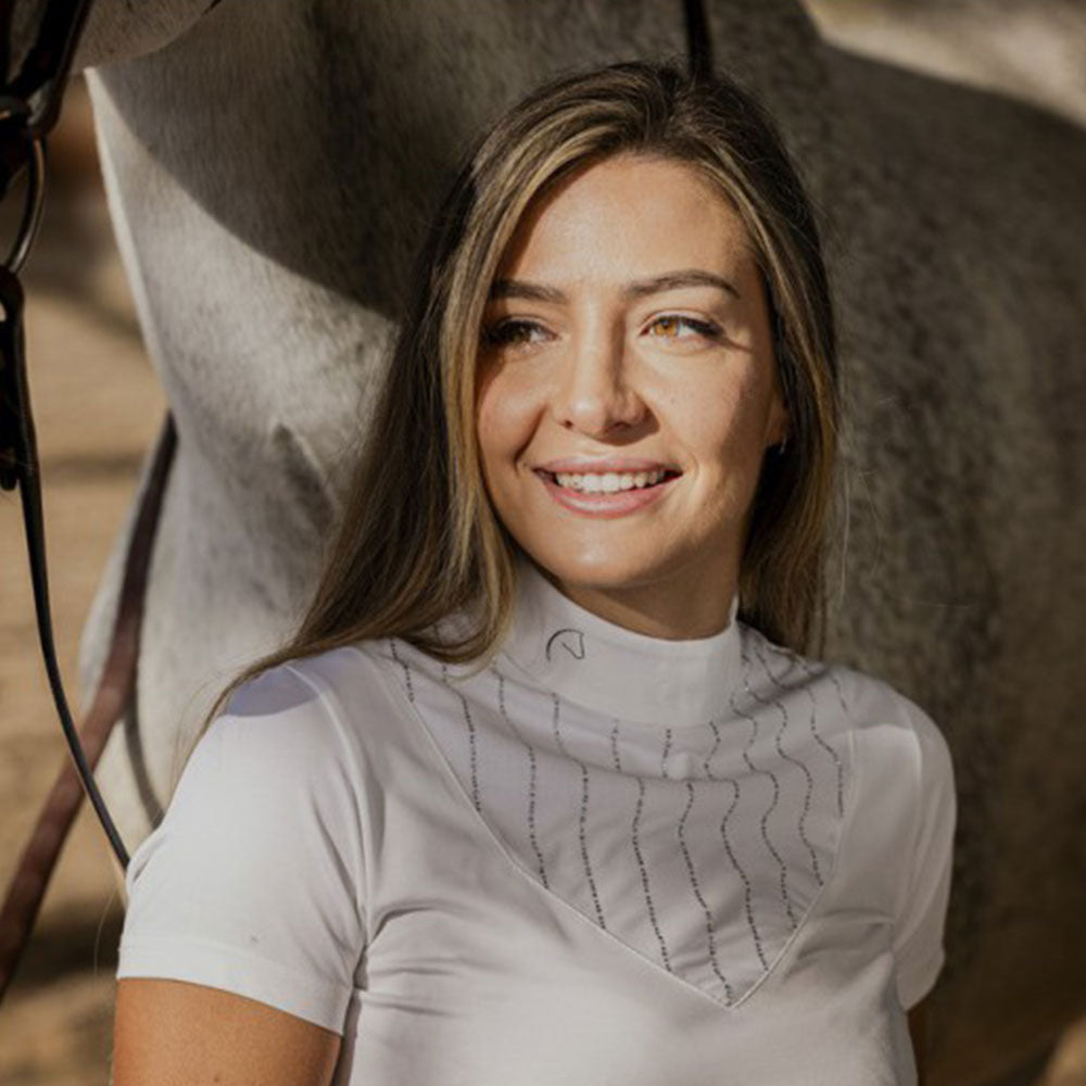 Woman standing next to a horse, both in equestrian attire, with a warm, natural light setting.