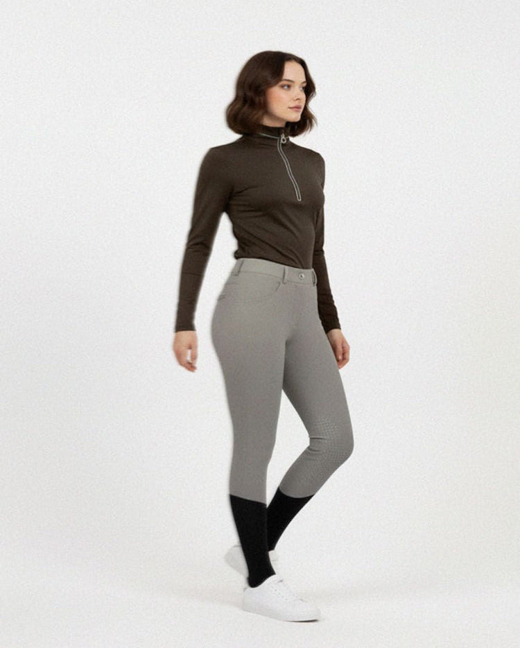 Woman wearing a brown long-sleeve top and gray riding pants on a white background