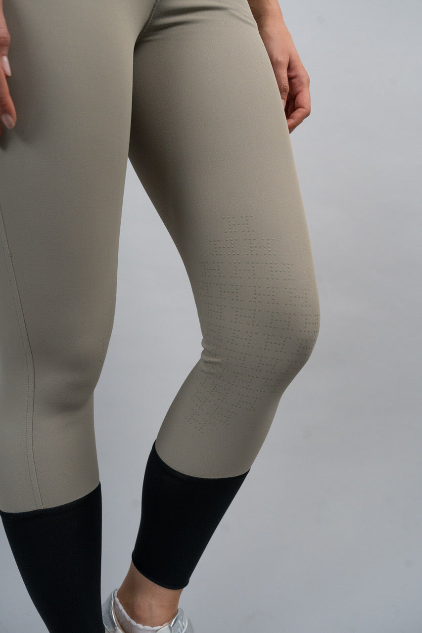 Beige riding leggings with black accents worn by a person on a plain background