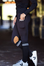 Person wearing dark blue equestrian leggings with a pocket, white sneakers, and a blurred background.