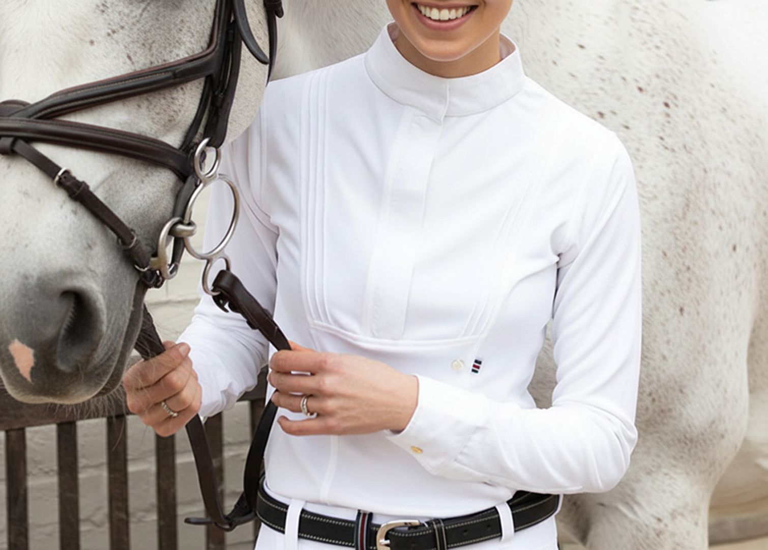 Person in a white equestrian shirt standing next to a horse